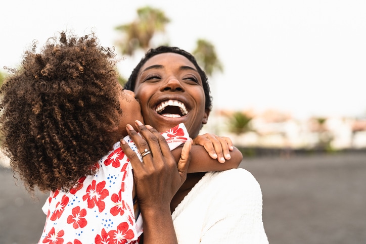 Happy mother laughing and embracing her young daughter who is kissing her on the cheek